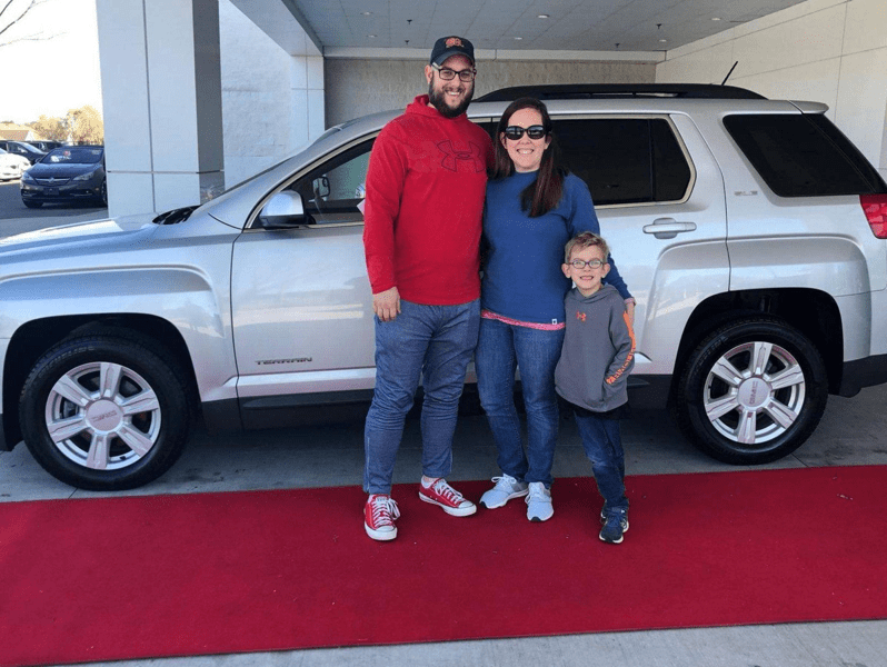 A young family poses in front of their leased silver GMC Terrain SUV