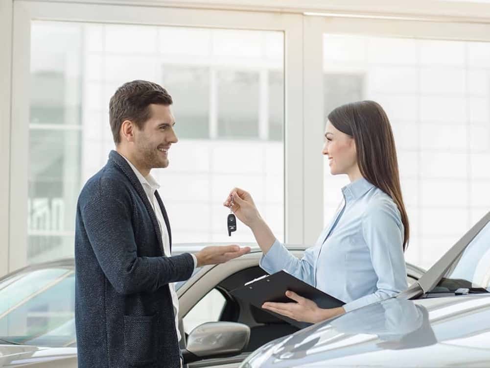 saleswoman-is-handing-car-keys-to-man-inside-showroom