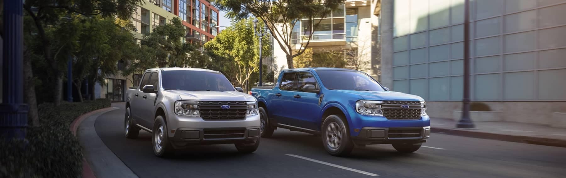 A silver and a blue Ford Truck driving down a city street mobile